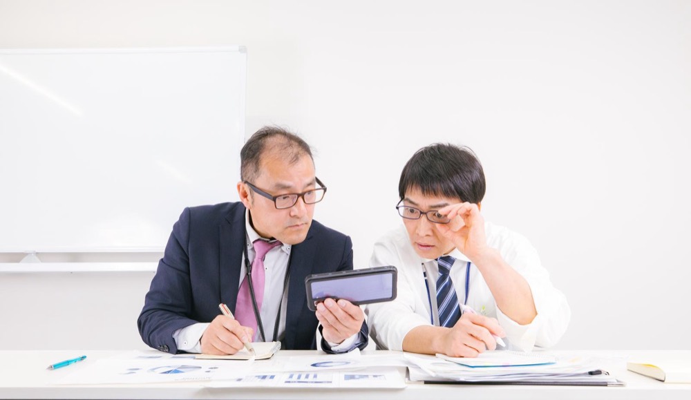 資料を見ながら新NISAについて話し合う会社員2人