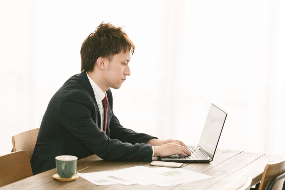 ノートパソコンで新NISAについて調べものをする会社員男性